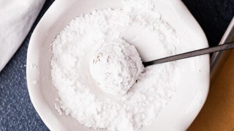 Molasses cookie rolled through powdered sugar in a white bowl.
