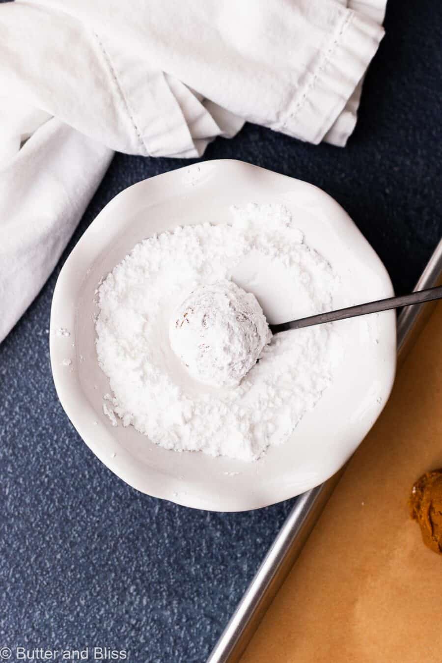Molasses cookie rolled through powdered sugar in a white bowl.