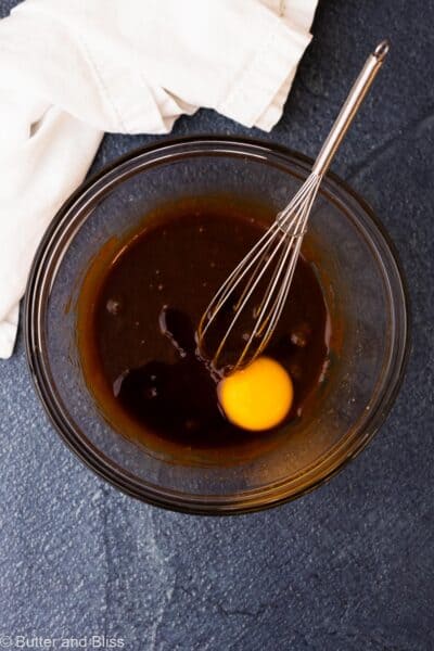 Egg yolk added to a mixing bowl of combined molasses and sugar.