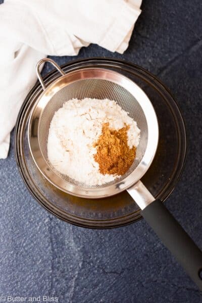 Dry cookie ingredients being sifted over a mixing bowl.