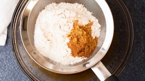 Dry cookie ingredients being sifted over a mixing bowl.