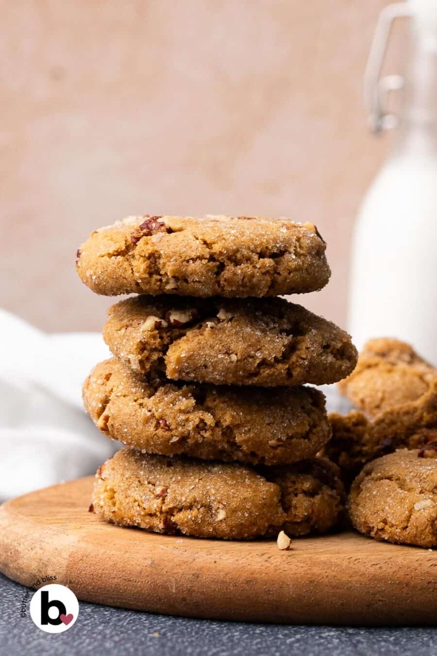 Small stack of thick pecan brown sugar cookies on a wood plate next to a glass of milk.