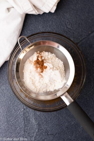 Dry cookie ingredients being sifted into a mixing bowl.