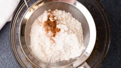 Dry cookie ingredients being sifted into a mixing bowl.