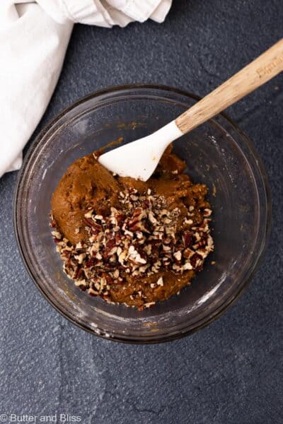 Chopped pecans added to a mixing bowl of thick cookie dough.