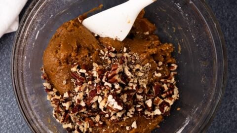 Chopped pecans added to a mixing bowl of thick cookie dough.