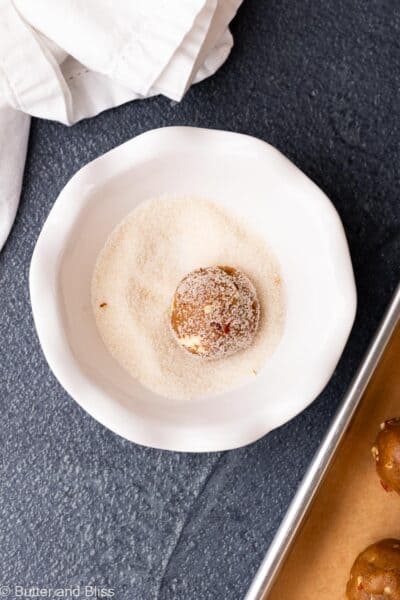 Brown sugar pecan cookie dough ball being rolled through sugar in a bowl.