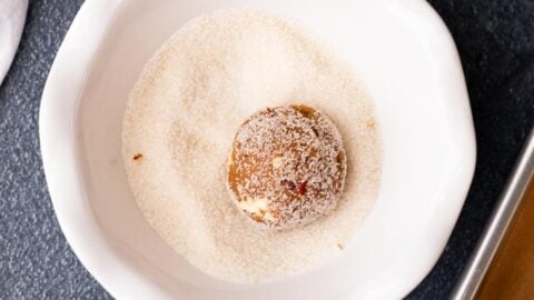 Brown sugar pecan cookie dough ball being rolled through sugar in a bowl.