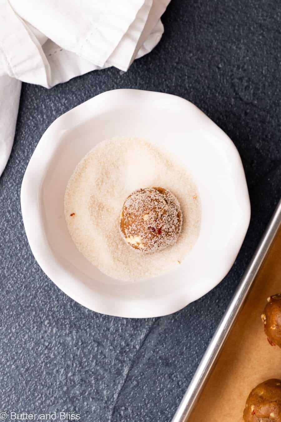 Brown sugar pecan cookie dough ball being rolled through sugar in a bowl.