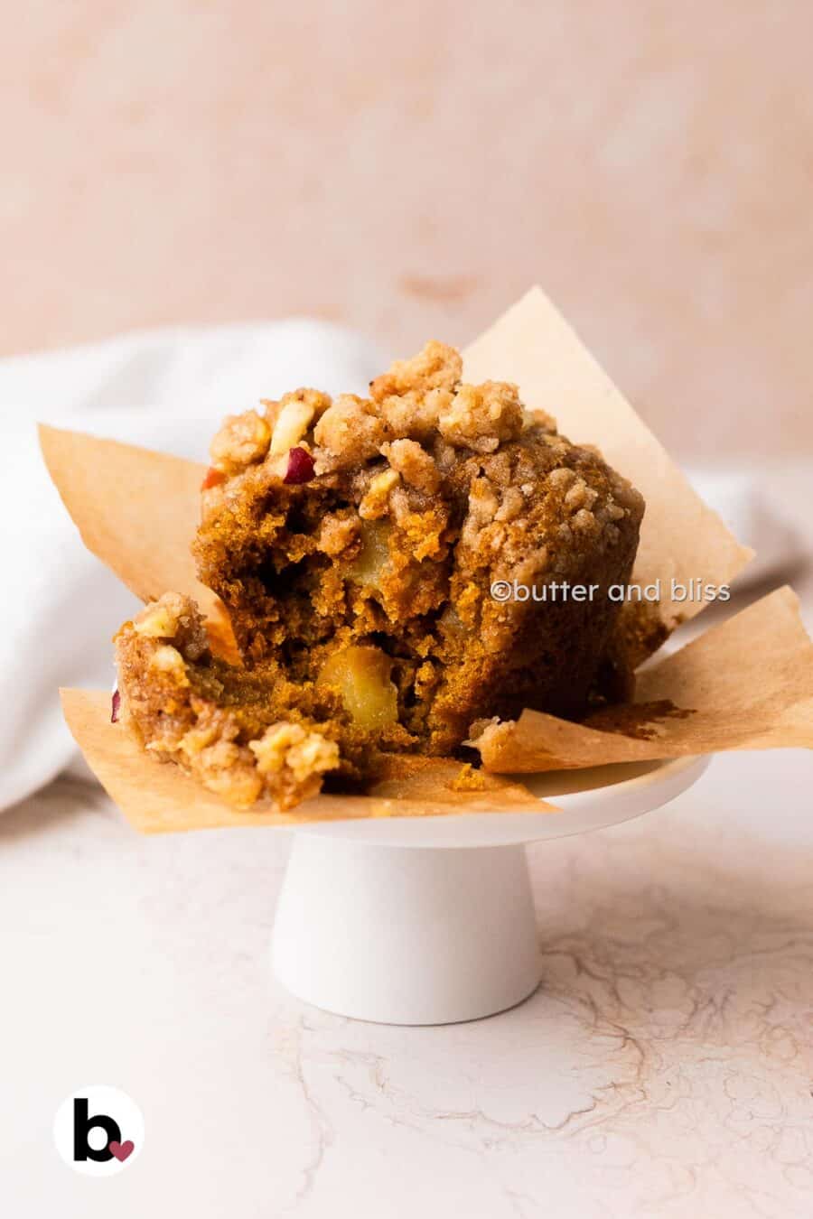 A apple pumpkin muffin with a bite taken to reveal the moist center and apple chunks.