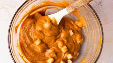 Pumpkin muffin batter with chunks of apple in a mixing bowl.