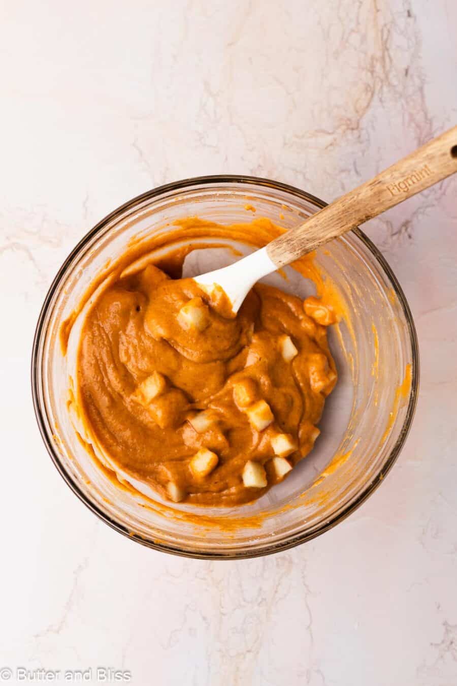 Pumpkin muffin batter with chunks of apple in a mixing bowl.