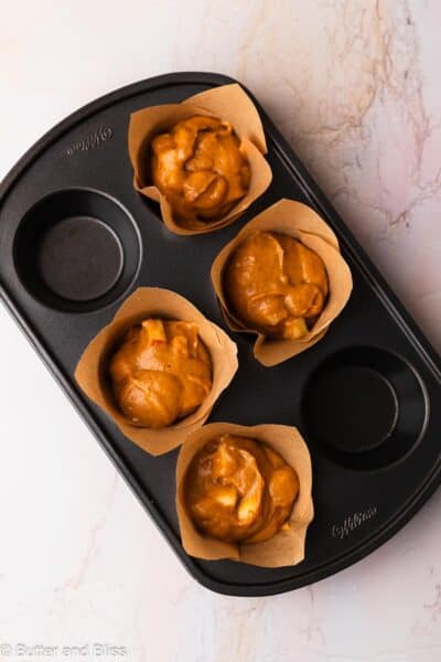 Apple pumpkin muffin batter in tulip liners in a muffin pan, ready to be baked.