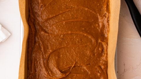 Pumpkin bar batter spread into a small baking sheet with an offset spatula.