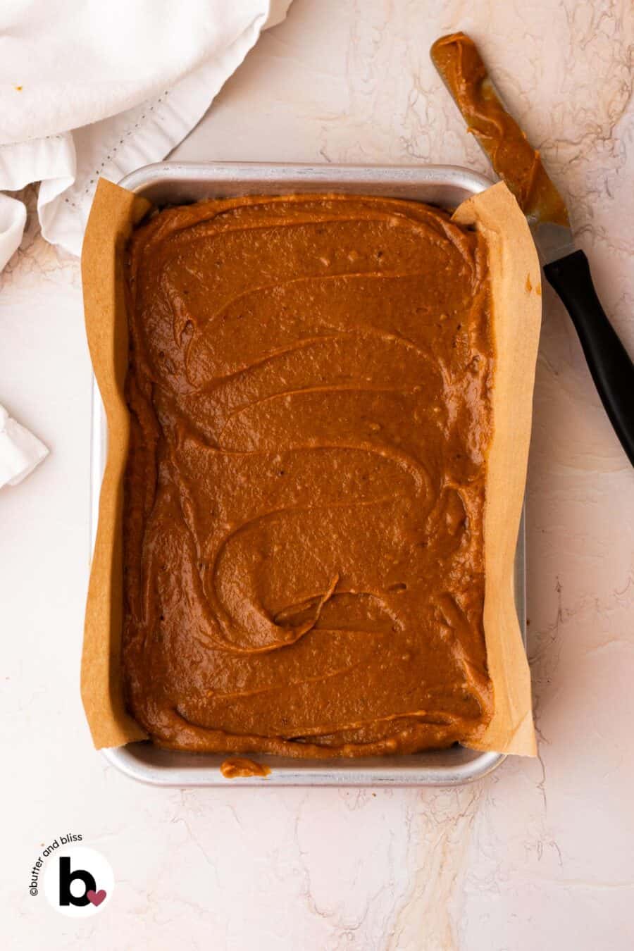 Pumpkin bar batter spread into a small baking sheet with an offset spatula.