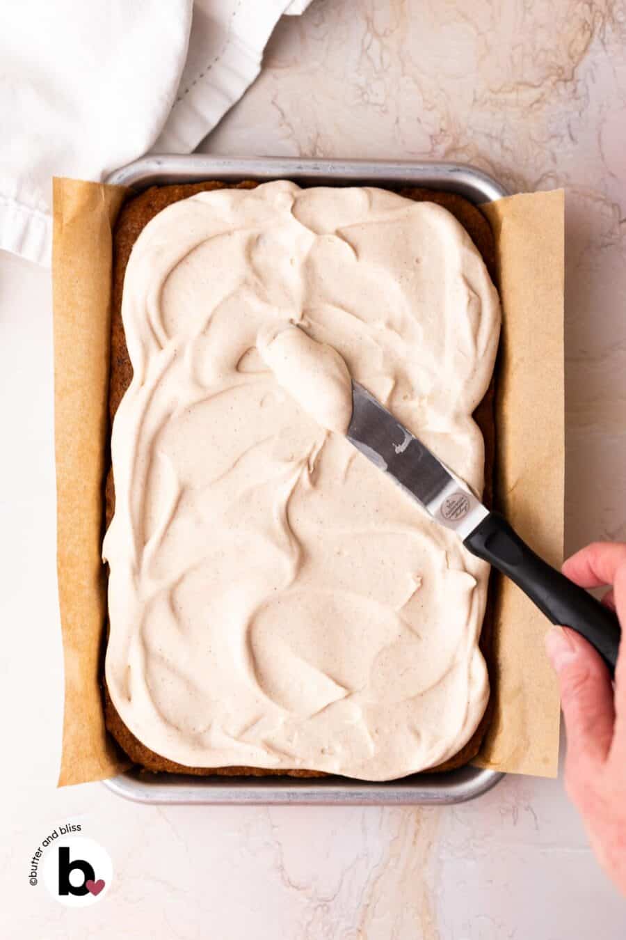 Hand spreading on cream cheese frosting onto pumpkin bars in a small pan.