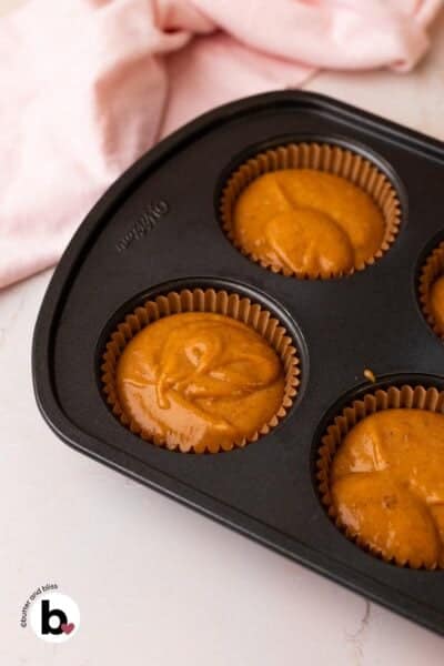 Pumpkin cupcake batter portioned into cupcake liners in a pan.