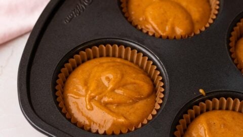 Pumpkin cupcake batter portioned into cupcake liners in a pan.