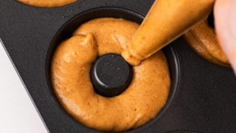 Pumpkin donut batter being piped into the wells of a donut pan.
