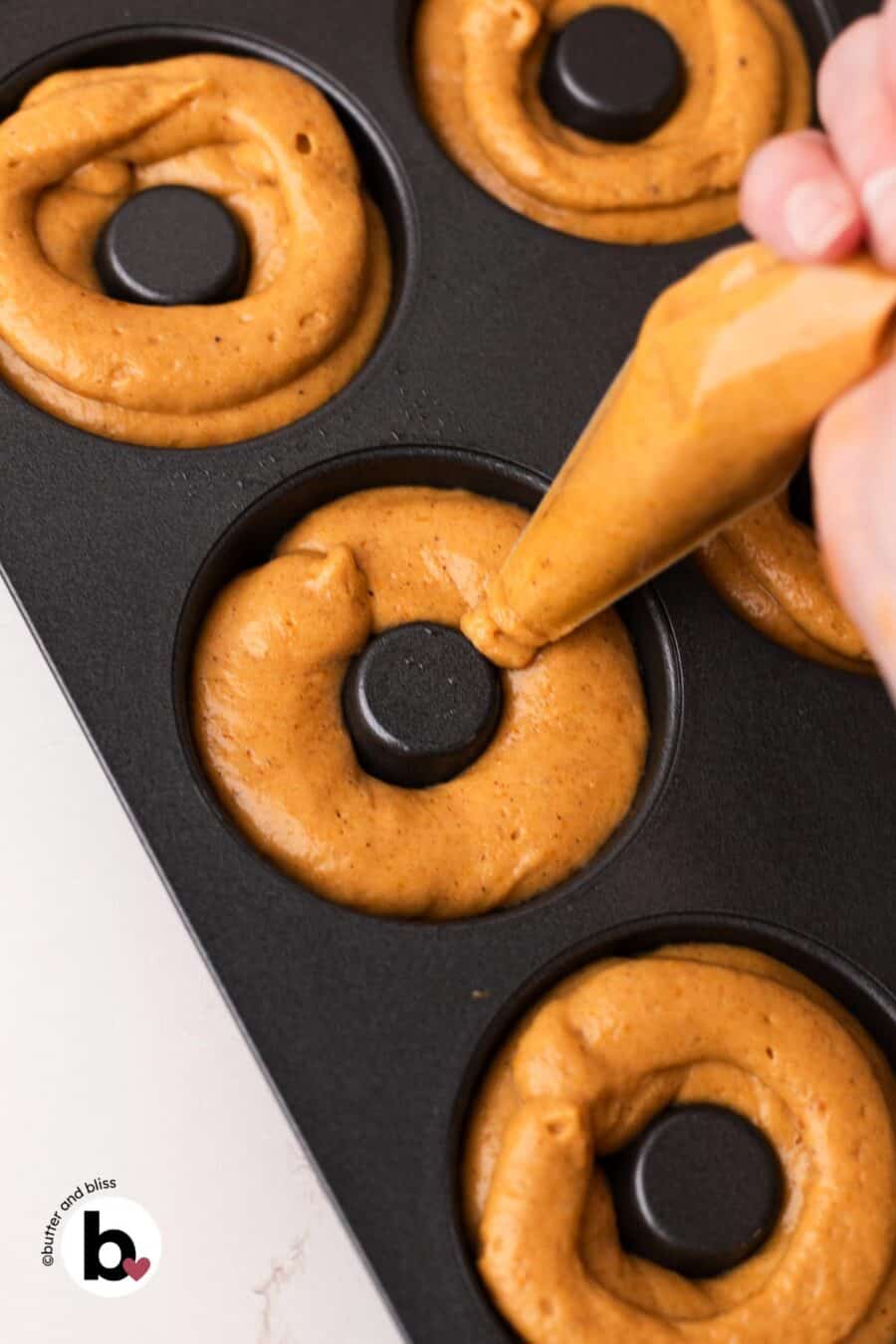 Pumpkin donut batter being piped into the wells of a donut pan.