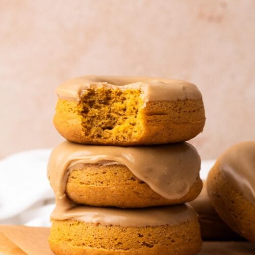 A stack of three pumpkin glazed donuts with a bite taken out of the top donut.