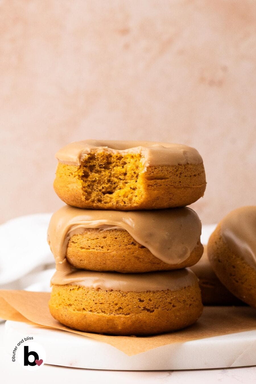 A stack of three pumpkin glazed donuts with a bite taken out of the top donut.