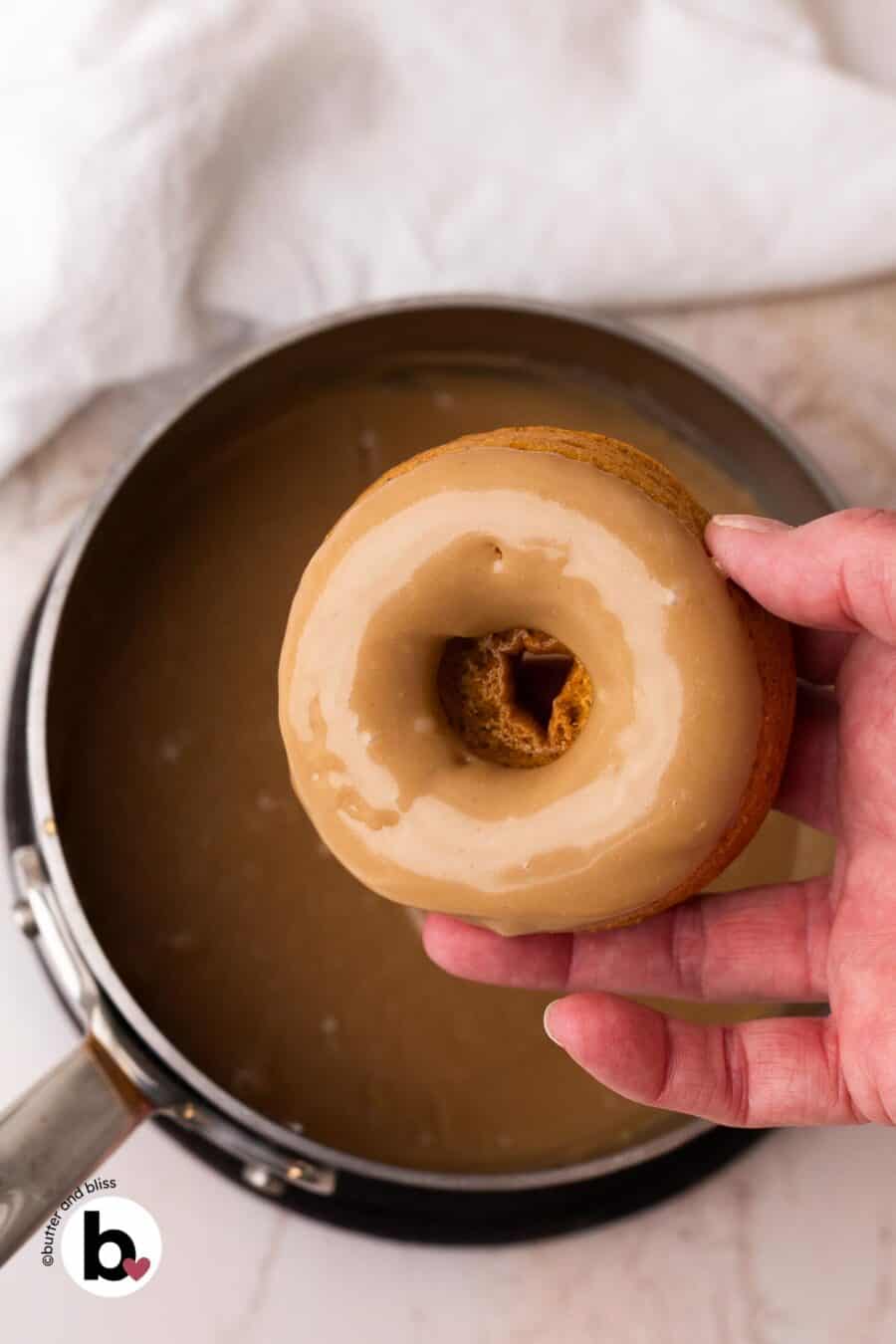 Hand holding a donut that has been dunked in shiny maple glaze.