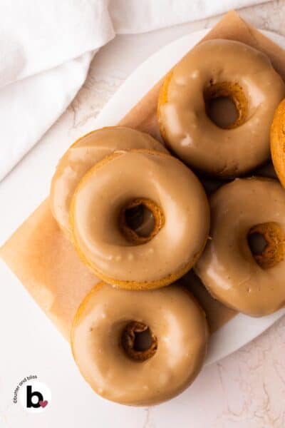 Small batch maple glazed pumpkin donuts stacked on a marble platter.