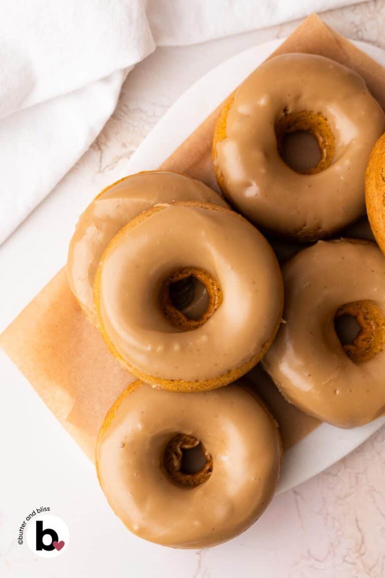 Small batch maple glazed pumpkin donuts stacked on a marble platter.