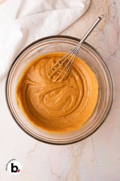 Smooth pumpkin muffin batter in a mixing bowl with a whisk.