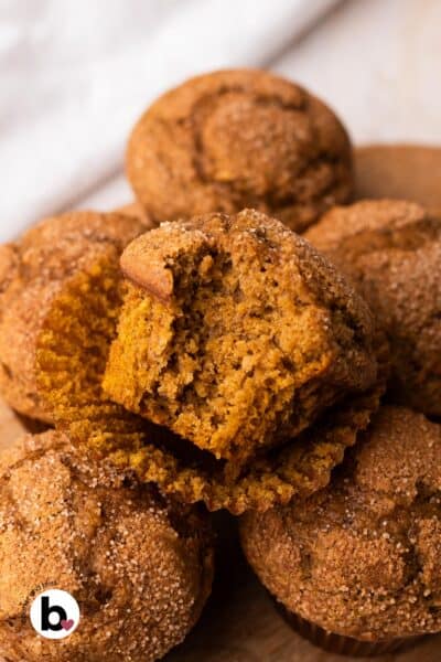 A pile of small batch pumpkin muffins with a bite taken out of the top one to reveal the moist center.