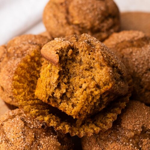 A pile of small batch pumpkin muffins with a bite taken out of the top one to reveal the moist center.