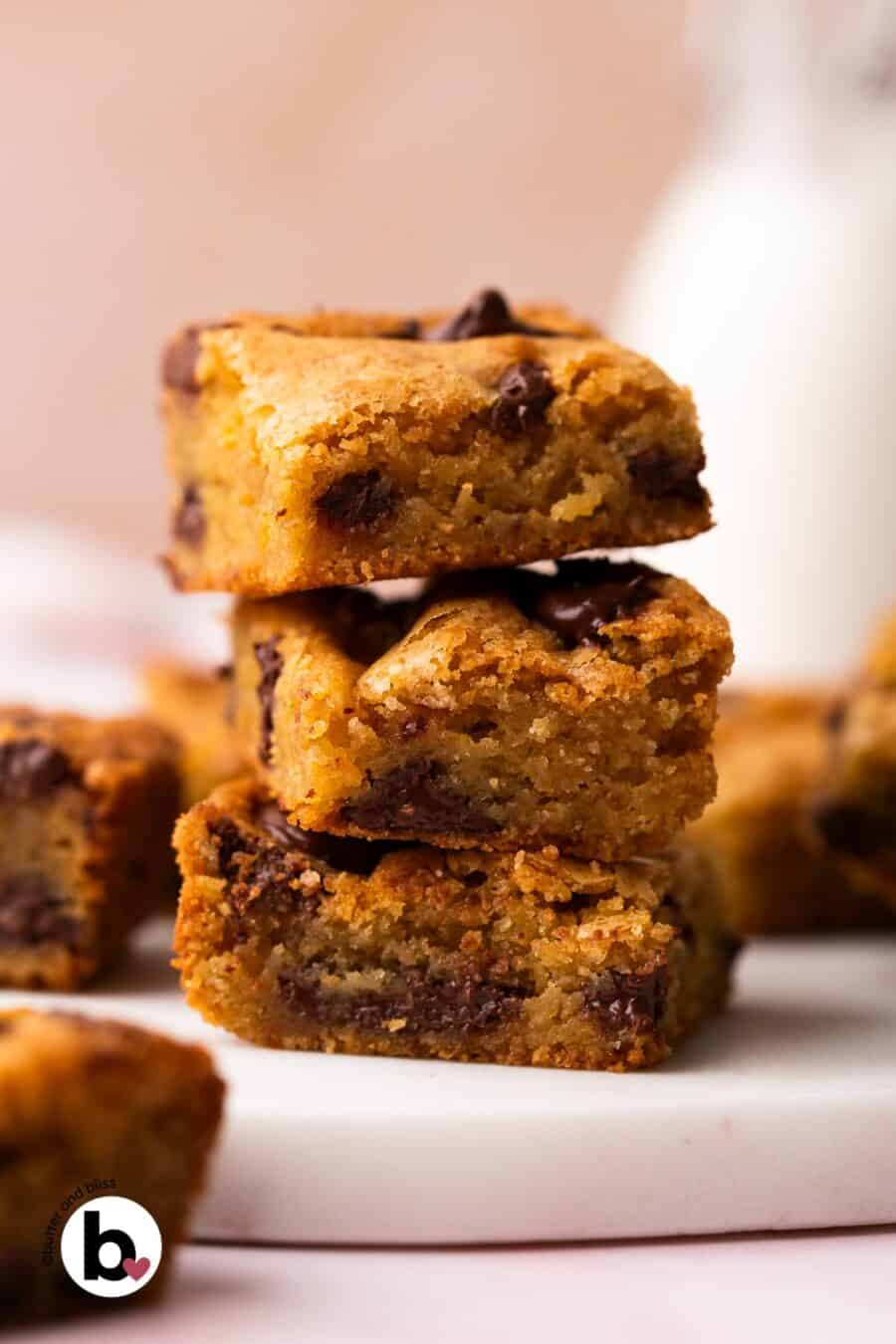 A small stack of gooey blondies with melty chocolate chips on a white marble plate.