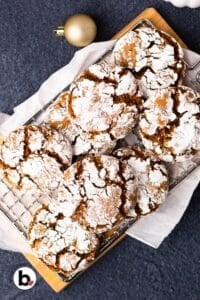 Fresh baked molasses crinkle cookies piled on a wood cutting board.