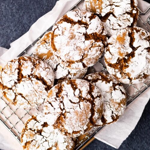 Fresh baked molasses crinkle cookies piled on a wood cutting board.