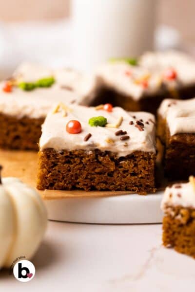 Single pumpkin bar square with cream cheese frosting and sprinkles on a marble plate.