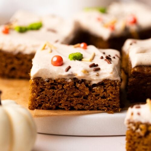 Single pumpkin bar square with cream cheese frosting and sprinkles on a marble plate.