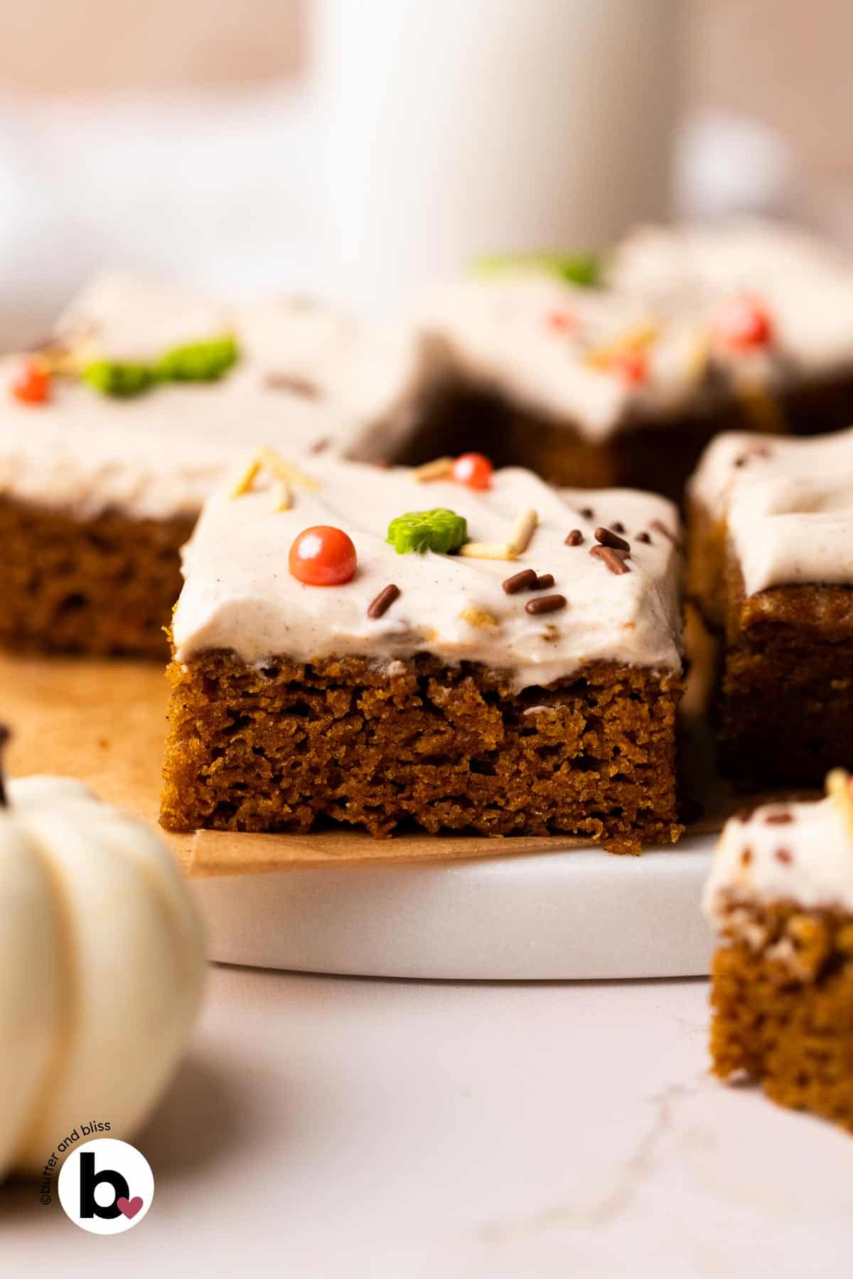 Single pumpkin bar square with cream cheese frosting and sprinkles on a marble plate.