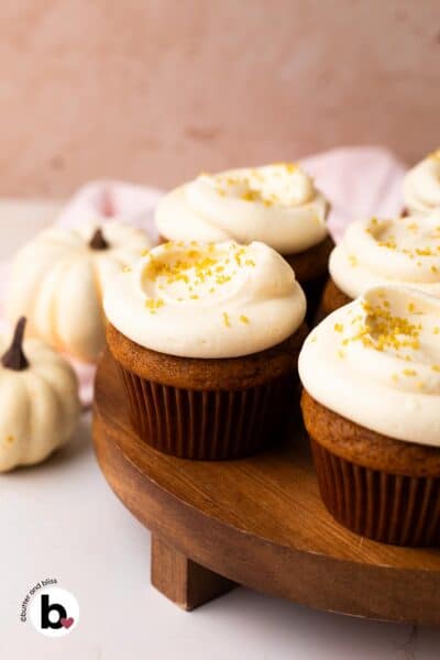 Small batch of pumpkin cupcakes with cream cheese frosting on a wood cake platter.