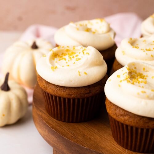 Small batch of pumpkin cupcakes with cream cheese frosting on a wood cake platter.