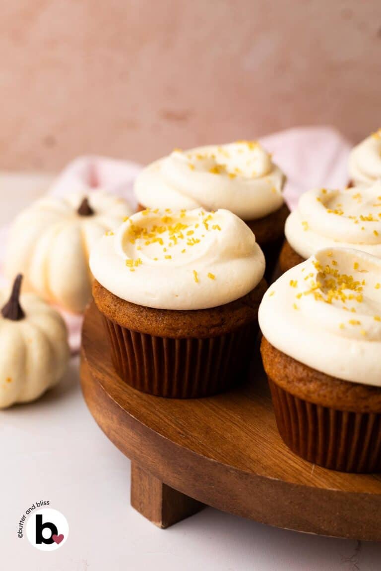 Small batch of pumpkin cupcakes with cream cheese frosting on a wood cake platter.
