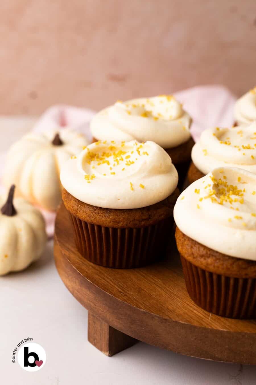 Small batch of pumpkin cupcakes with cream cheese frosting on a wood cake platter.
