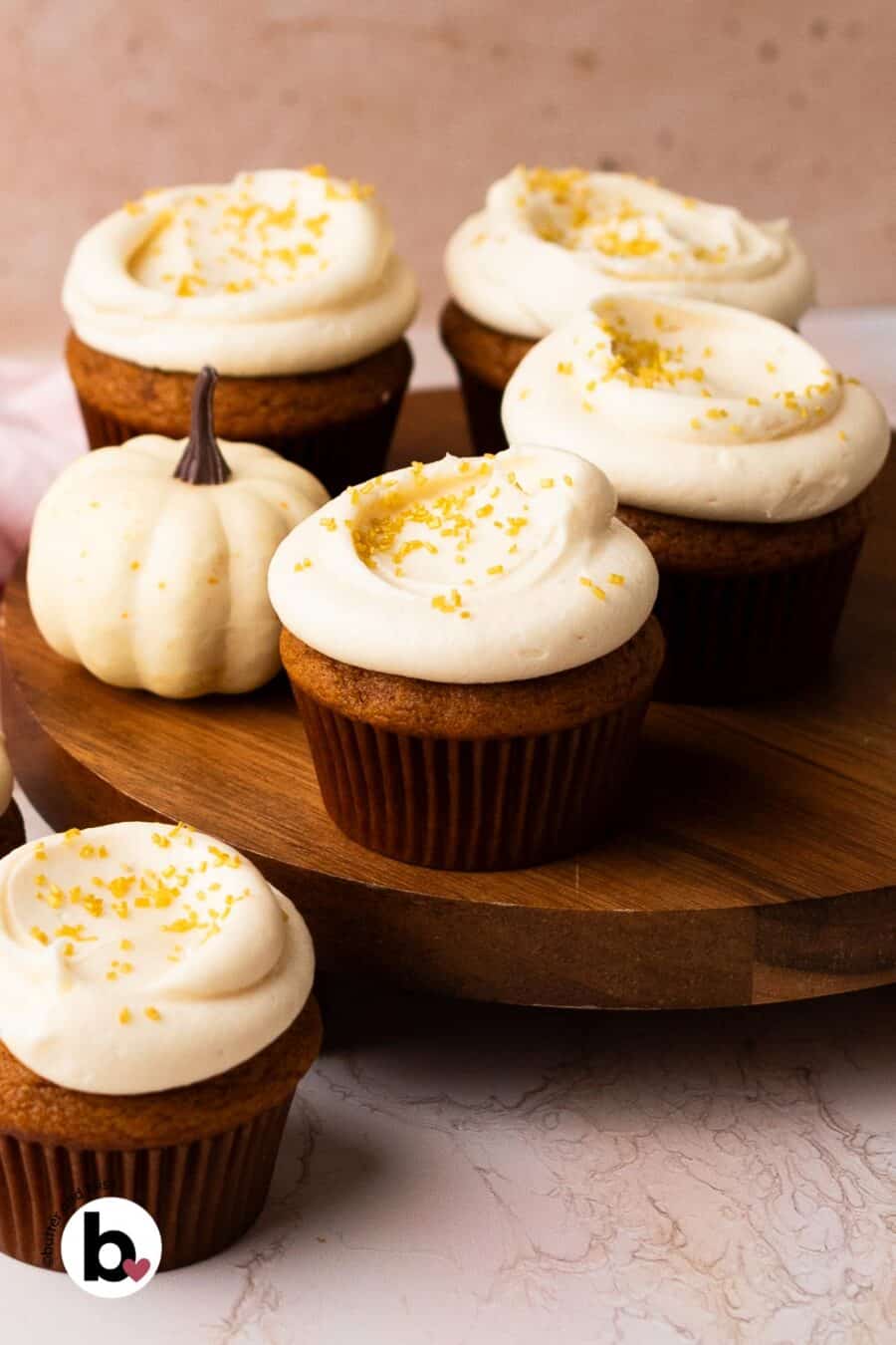 Frosted pumpkin cupcakes on a wood cake platter.