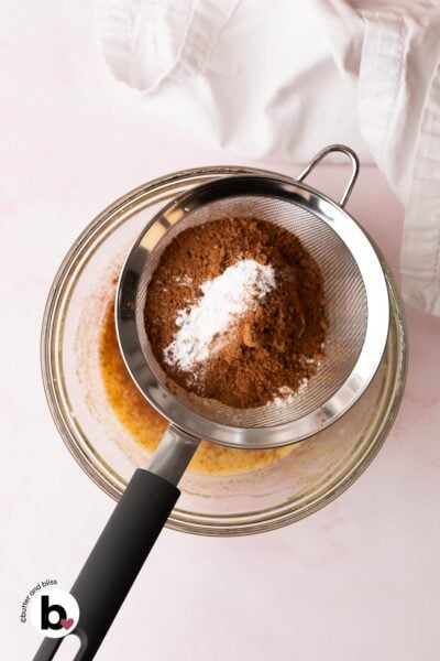 Dry ingredients being sifted over a bowl of wet cookie ingredients.
