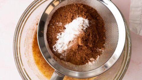 Dry ingredients being sifted over a bowl of wet cookie ingredients.