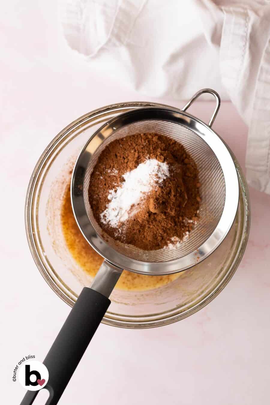Dry ingredients being sifted over a bowl of wet cookie ingredients.