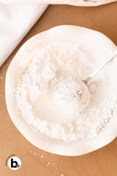 Chocolate cookie dough ball rolled through a bowl of powdered sugar.