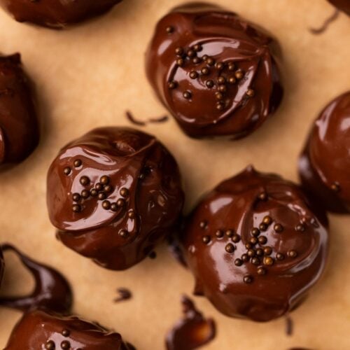 Chocolate covered cookie dough bites with chocolate sprinkles on a baking sheet.