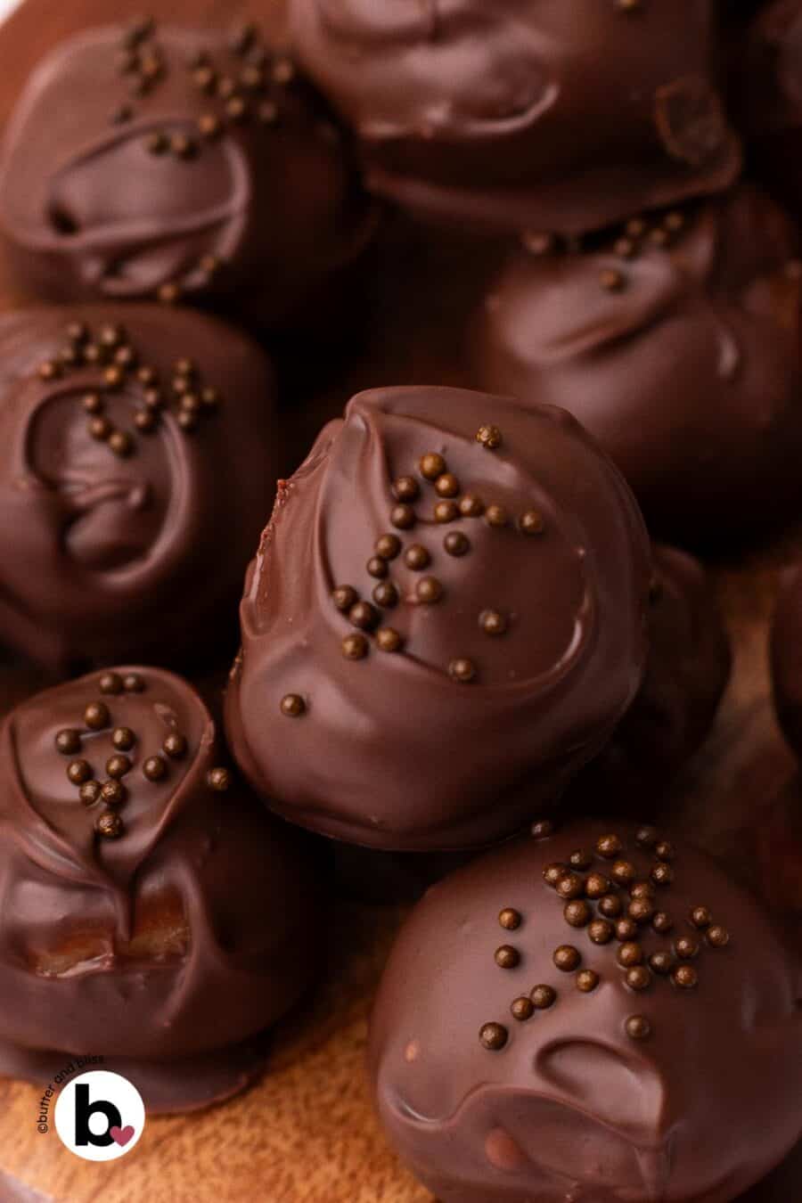Pile of chocolate covered cookie dough bites with chocolate sprinkles on a wood plate.