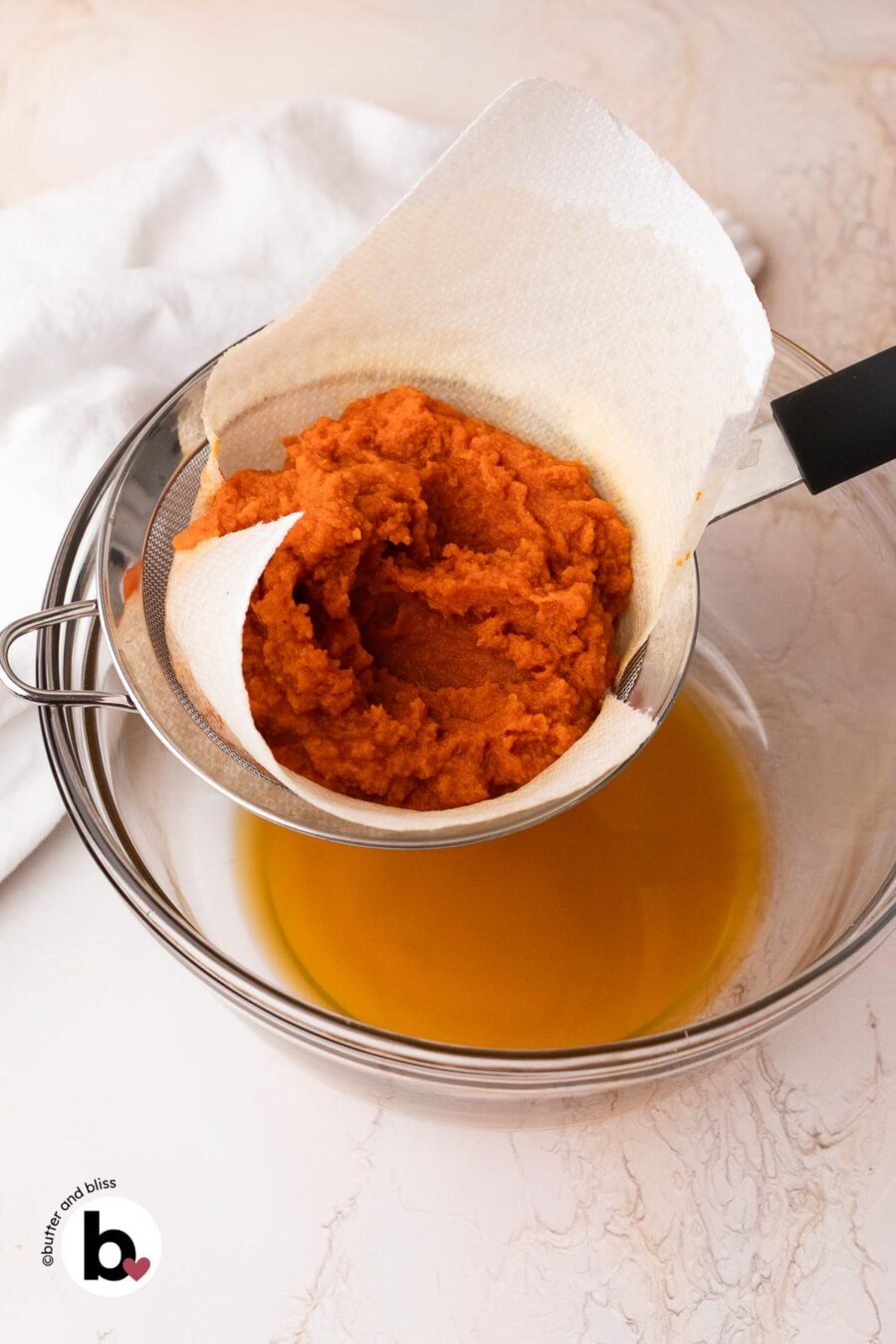 Leftover pumpkin puree being drained into a bowl through a paper lined mesh strainer.